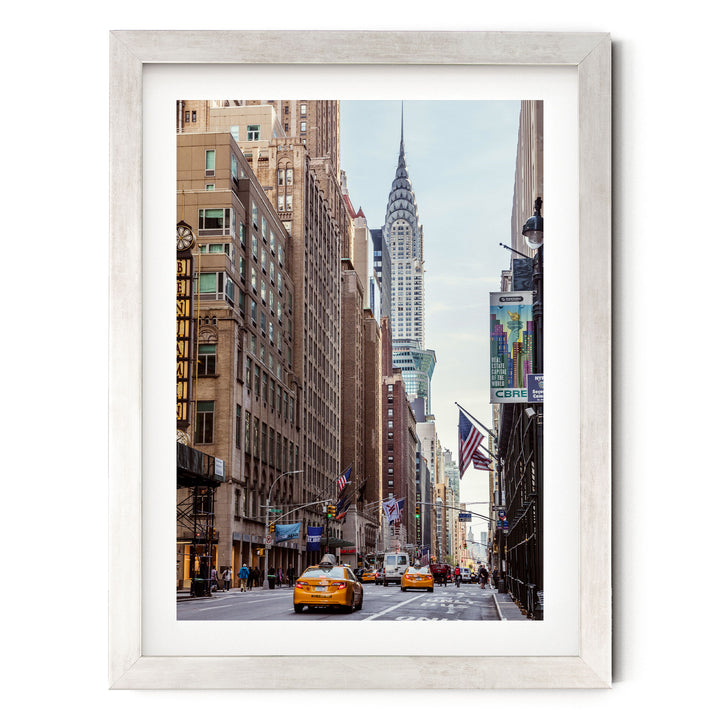 A framed photograph of a busy city street with tall buildings, including the iconic Chrysler Building, and yellow taxis driving down the road.