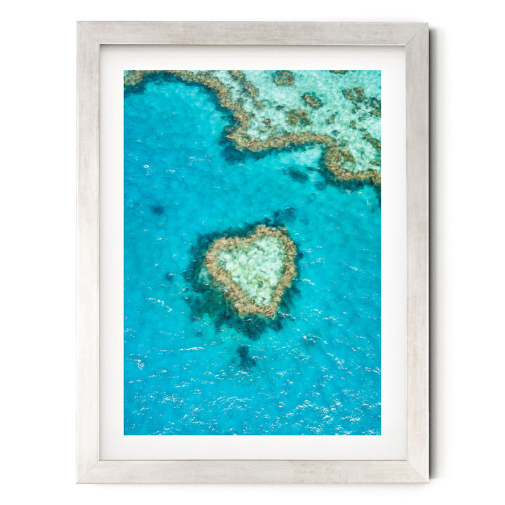The image is a framed aerial view of a coral reef, showcasing the vibrant blue waters and the intricate coral formations.