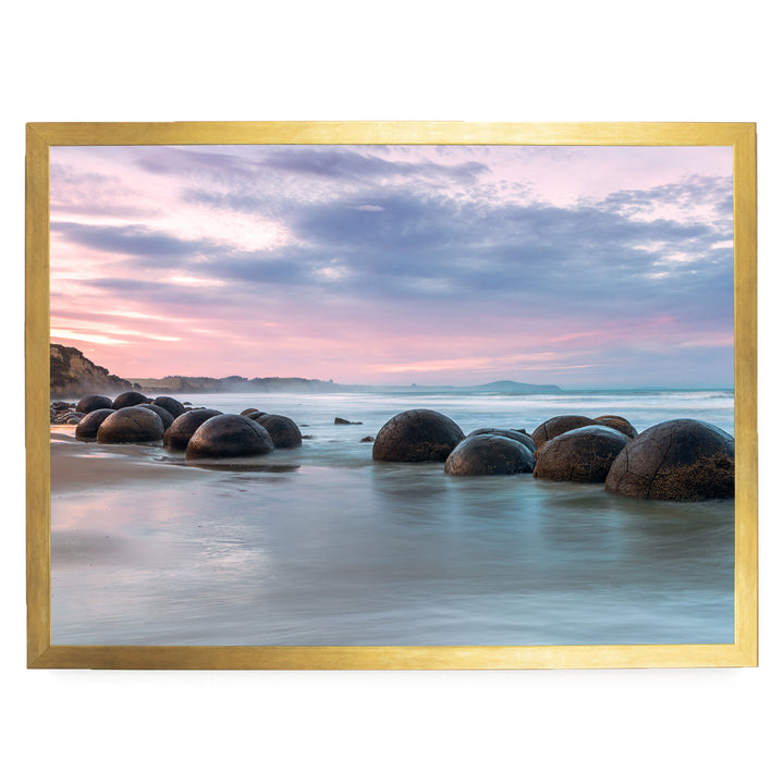 A serene beach scene with a collection of large, round boulders in the water, set against a backdrop of a colorful sunset sky.