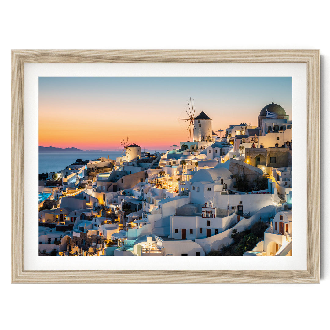 a picturesque coastal town with white buildings, windmills, and a stunning sunset over the water.