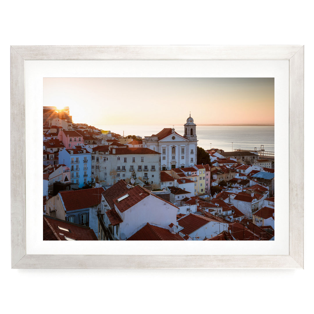 a picturesque town with a church and colorful buildings, set against a backdrop of a sunset over the ocean.