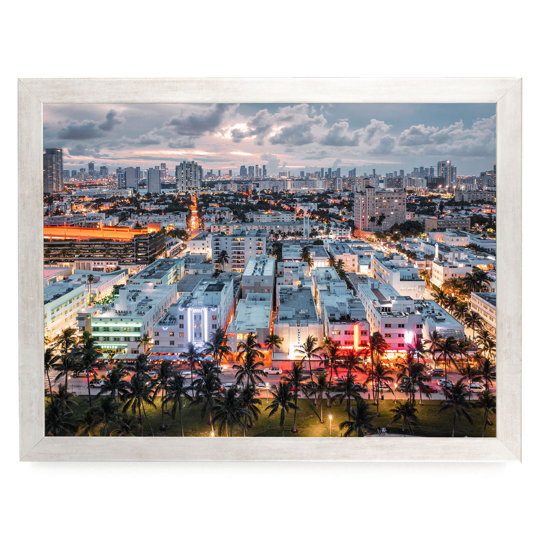 a vibrant cityscape at dusk, with a mix of tall buildings and palm trees illuminated by colorful lights.