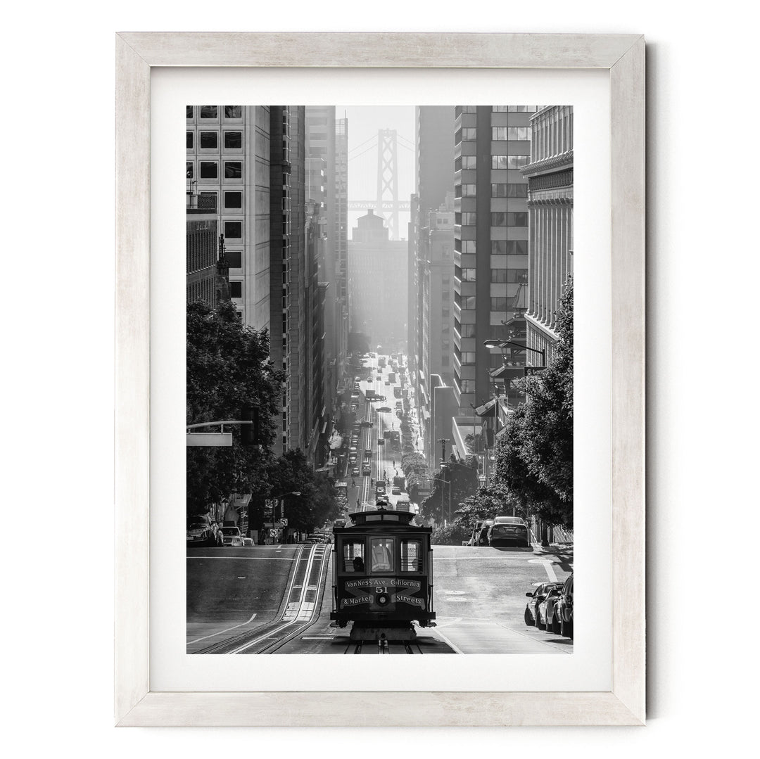 A black and white photograph of a trolley car traveling down a city street, surrounded by tall buildings and traffic.
