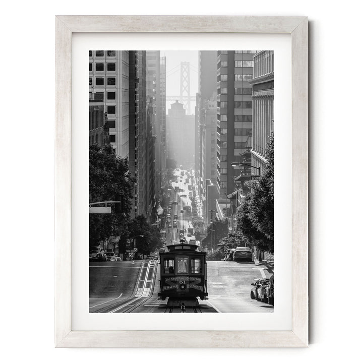 A black and white photograph of a trolley car traveling down a city street, surrounded by tall buildings and traffic.