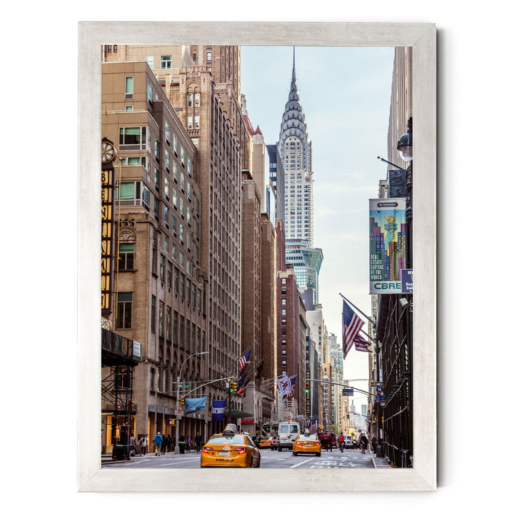 A bustling city street with tall buildings, including the iconic Chrysler Building, and yellow taxis driving down the road.