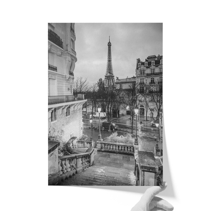 A black and white photograph of the Eiffel Tower in Paris, France, with a view of the surrounding buildings and a wet street below.