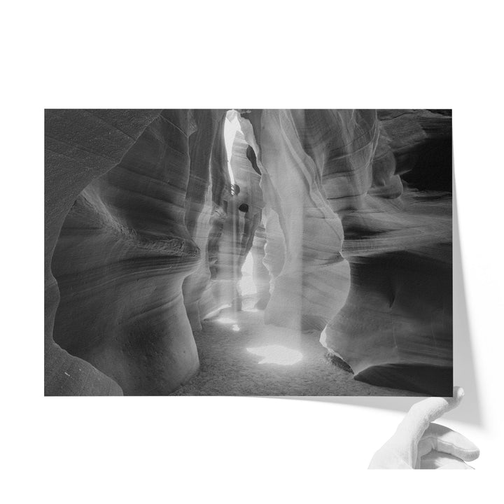 A black and white photograph of a narrow, winding path leading through a natural rock formation, with sunlight filtering through the rock.
