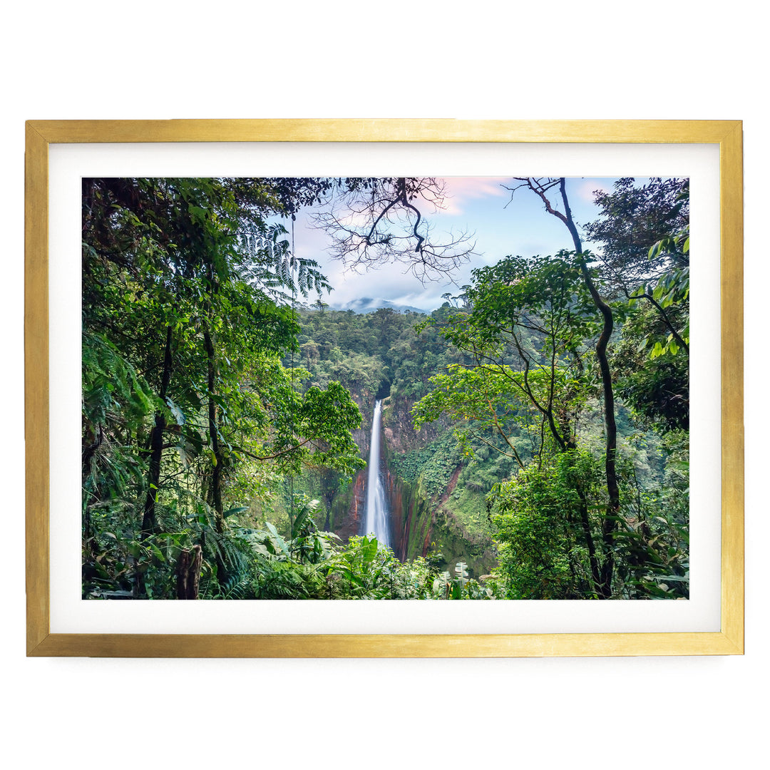 A lush, verdant forest with a majestic waterfall cascading down the rocky cliff face, framed in a gold frame.