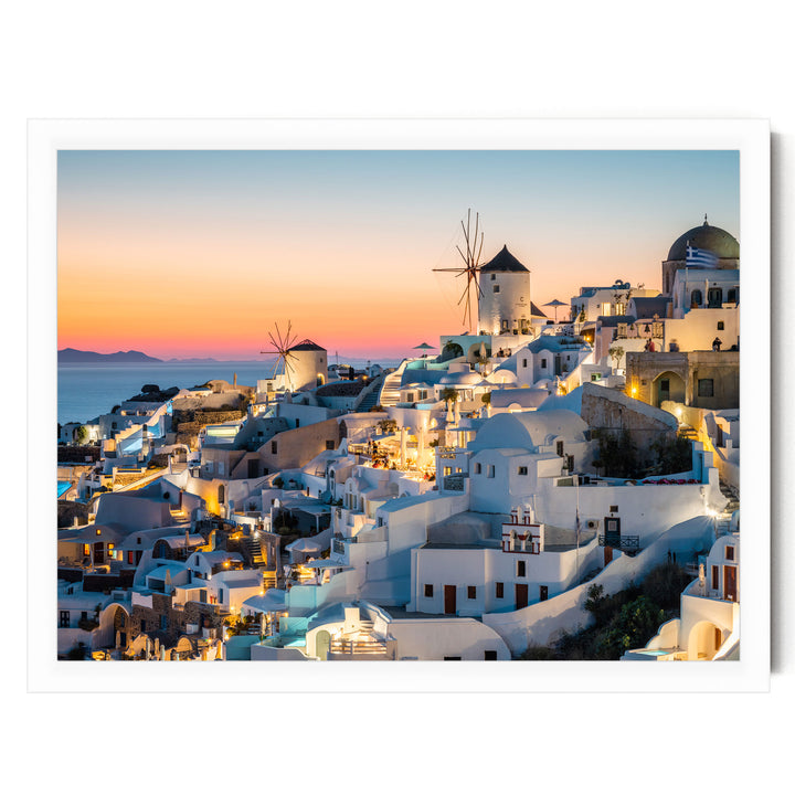 a picturesque coastal town with white buildings and windmills, illuminated at night against a backdrop of a colorful sunset sky.