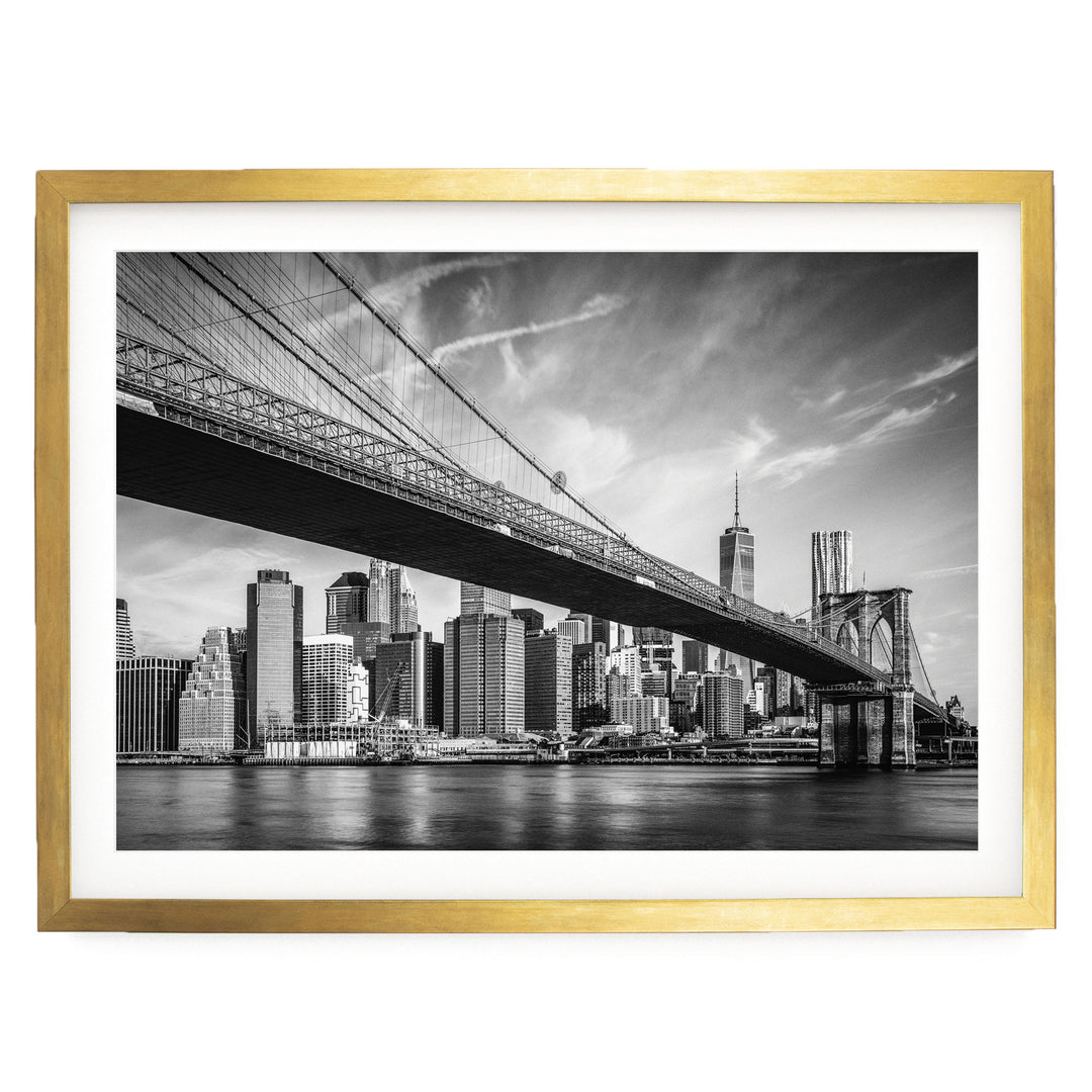 A black and white photograph of the Brooklyn Bridge spanning the East River, with the city skyline of New York City visible in the background.