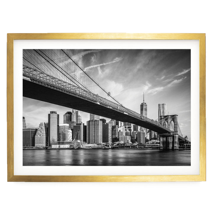 A black and white photograph of the Brooklyn Bridge spanning the East River, with the city skyline of New York City visible in the background.