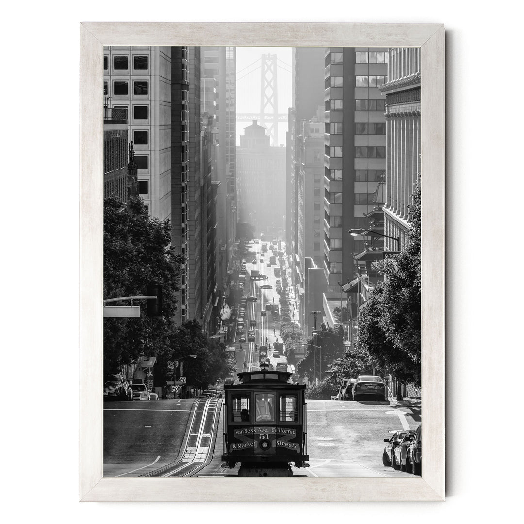 A black and white photograph of a trolley car traveling down a busy city street, surrounded by tall buildings and traffic.
