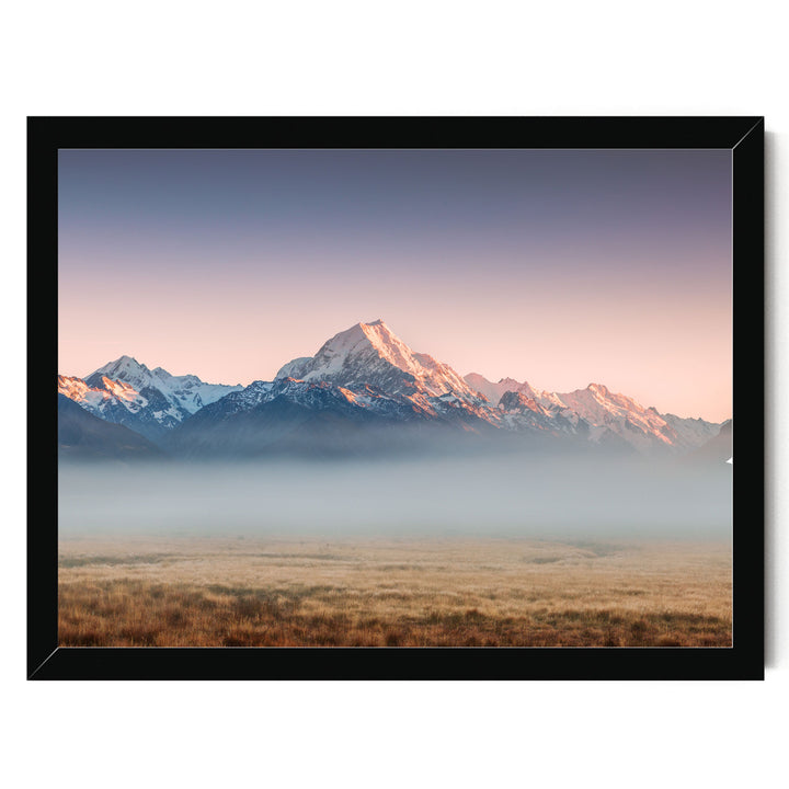 A breathtaking landscape featuring snow-capped mountains in the distance, with a hazy, golden-hued sky above. The mountains are partially obscured by a misty haze, creating a serene and atmospheric scene.
