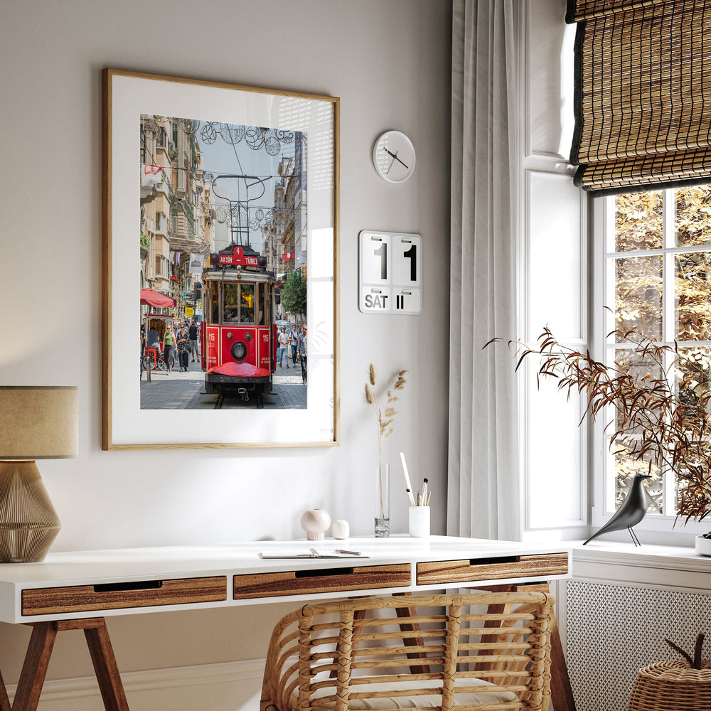 a modern, minimalist living space with a large framed picture of a red trolley car on the wall, a white desk with a lamp and a plant, and a window with a bird perched on it.