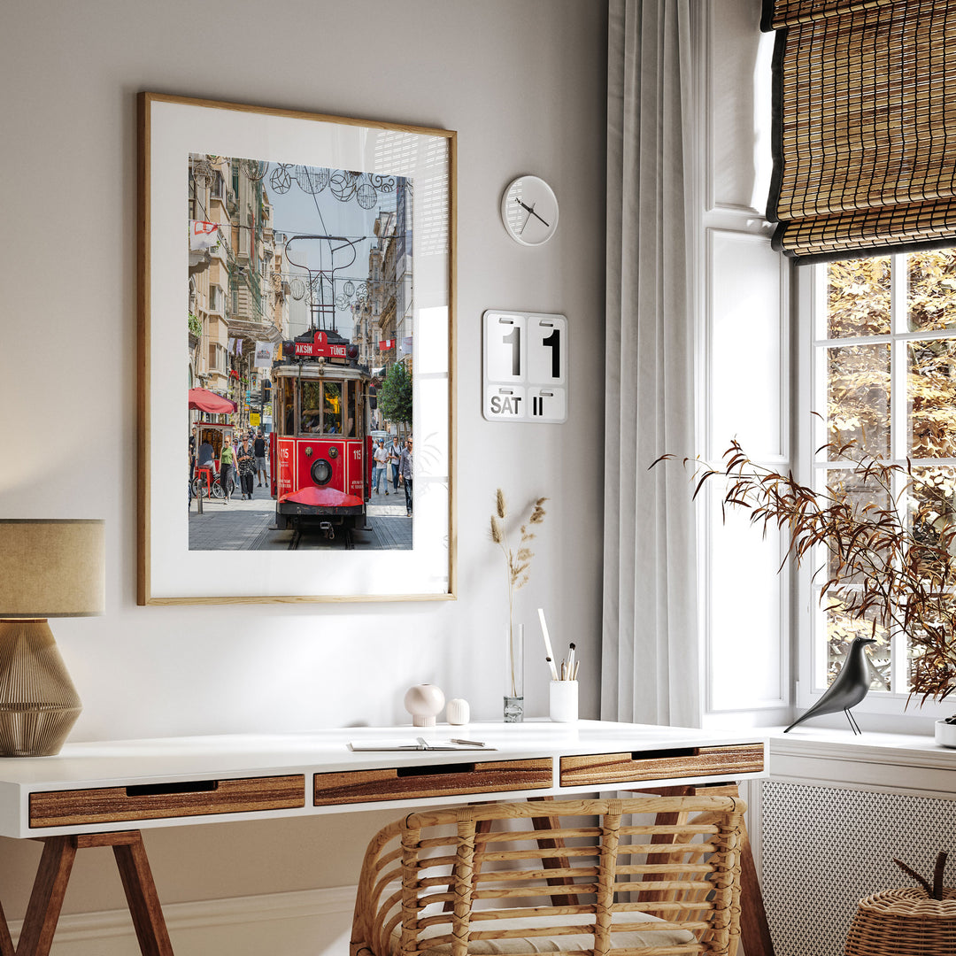 a modern, minimalist living space with a large framed picture of a red trolley car on the wall, a white desk with a lamp and a plant, and a window with a bird perched on it.