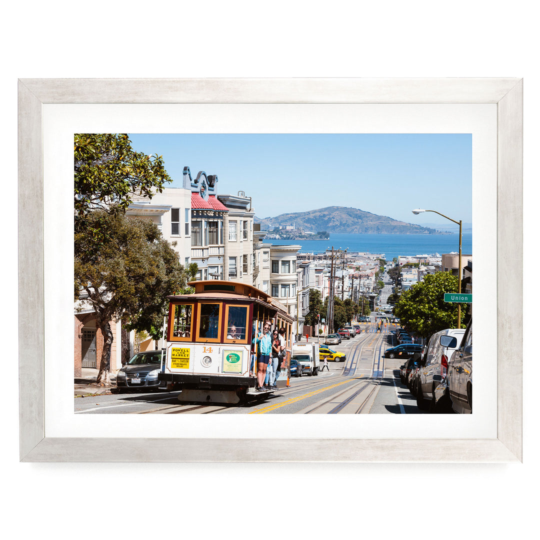 A cable car is traveling down a busy street in San Francisco, with buildings, cars, and pedestrians visible in the background.
