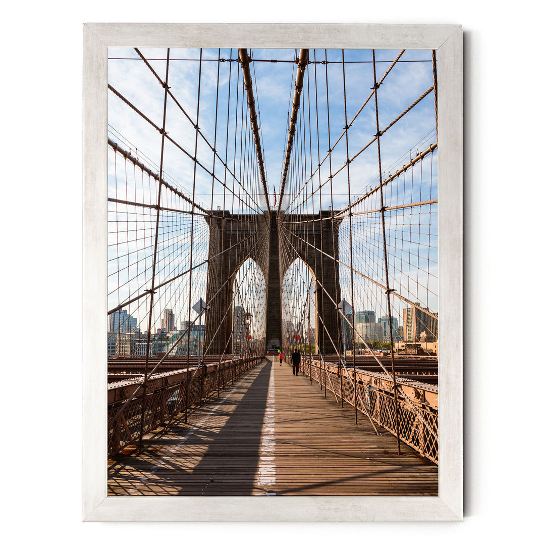 the iconic Brooklyn Bridge, with its distinctive Gothic-style towers and suspension cables, spanning across the frame. The bridge is viewed from the pedestrian walkway, providing a clear view of the structure and its surroundings.