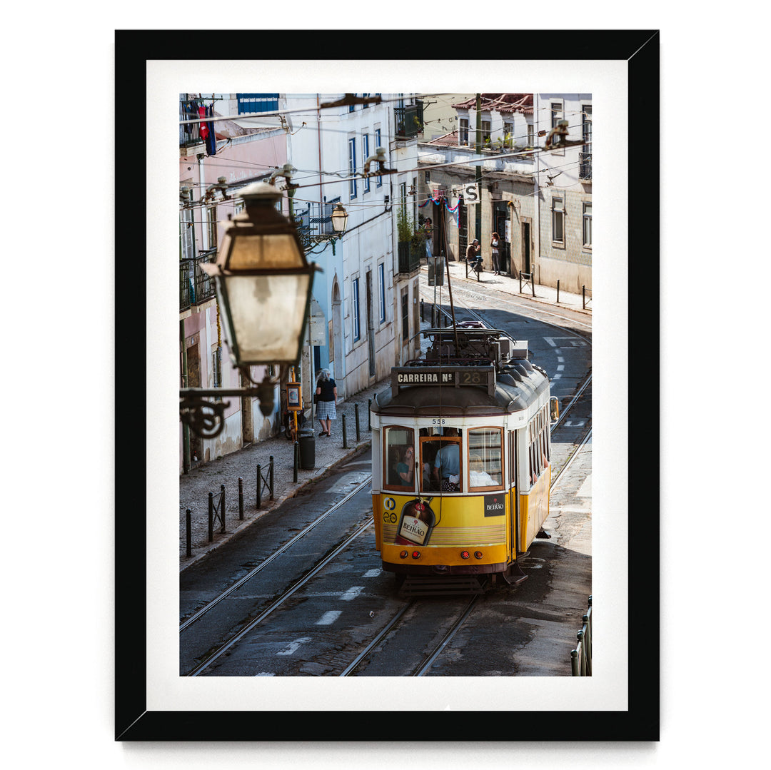 A yellow tram is traveling down a street lined with buildings and lampposts.