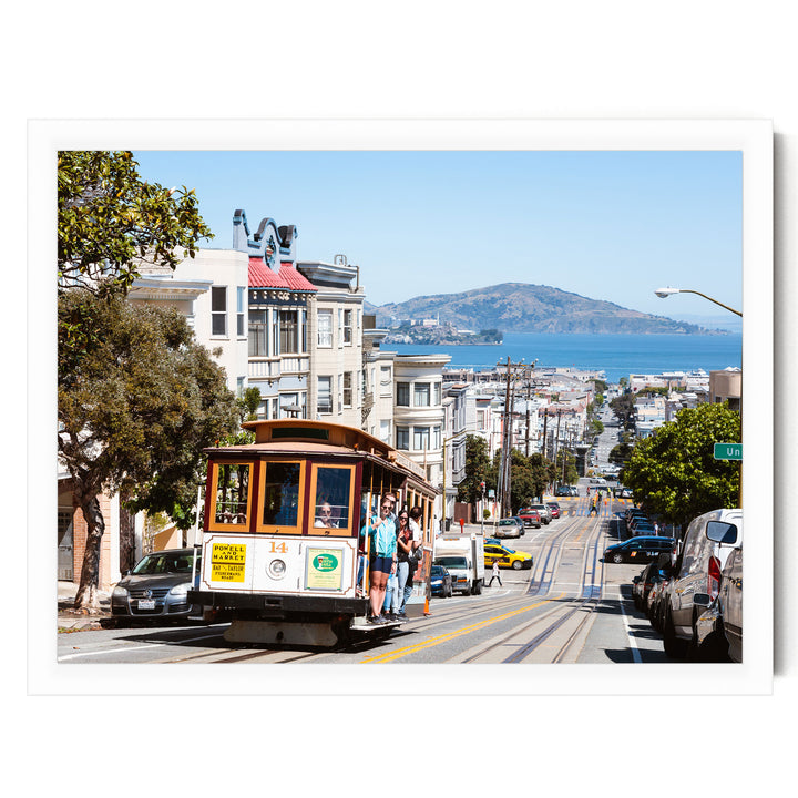 A cable car is traveling down a busy street in San Francisco, with buildings, cars, and pedestrians visible in the background.