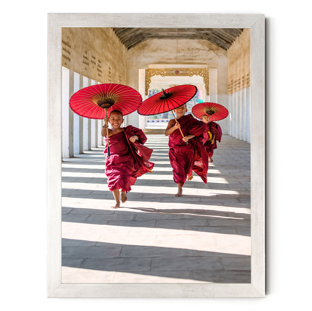 Three young monks in red robes are walking down a hallway, each holding a red umbrella.