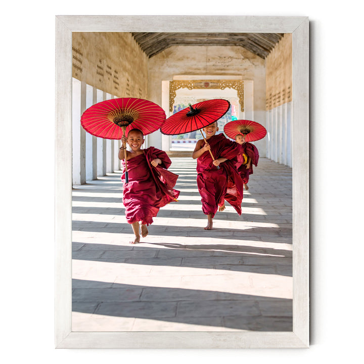 Three young monks in red robes are walking down a hallway, each holding a red umbrella.