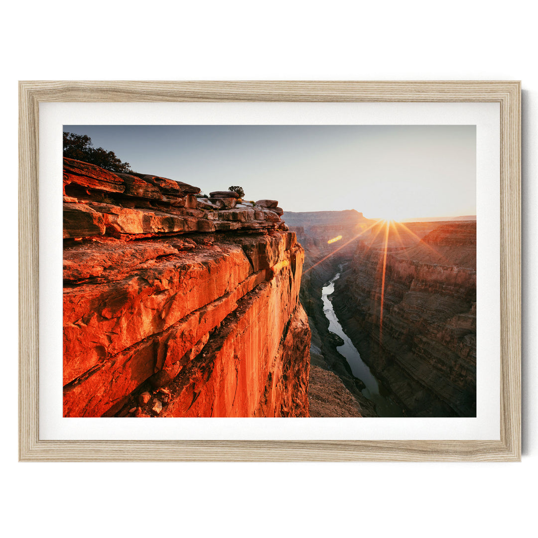 A framed photograph depicting a dramatic canyon landscape with a river flowing through it, set against a backdrop of a sunrise or sunset.