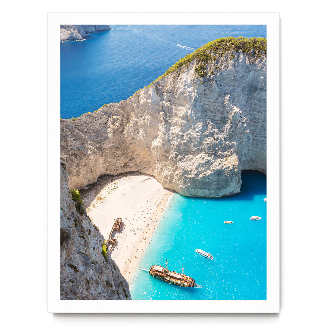 a picturesque coastal scene with a rocky cliff overlooking a beach and turquoise waters. Several boats are visible in the water, adding to the serene atmosphere.