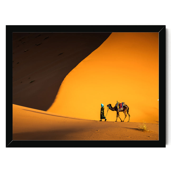 A camel and a person walking in a desert landscape with a large sand dune in the background.