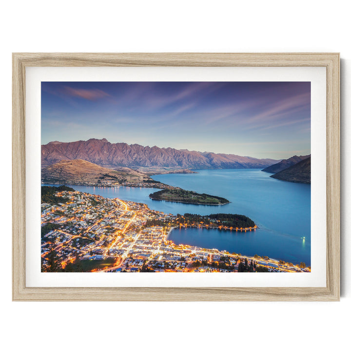 a picturesque town nestled at the foot of a mountain range, with the town's lights twinkling in the evening and the surrounding mountains bathed in a warm, golden glow.