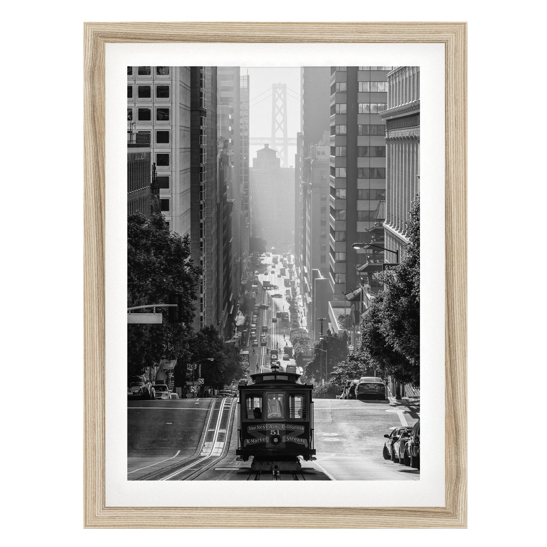 A black and white photograph of a trolley car traveling down a busy city street, surrounded by tall buildings and traffic.