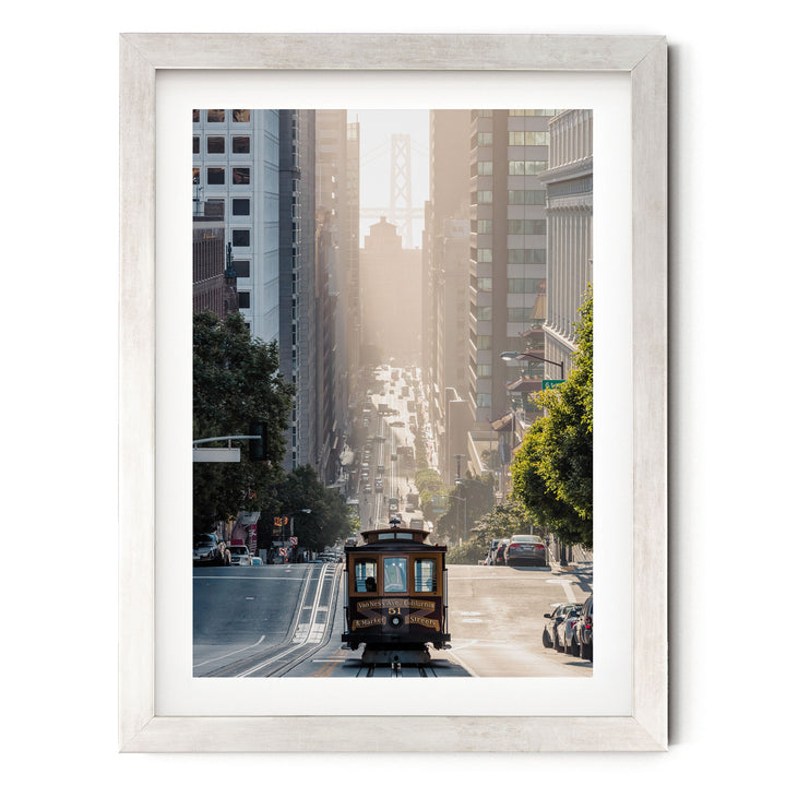 A framed photograph depicting a trolley car traveling down a city street, with tall buildings and trees lining the street.