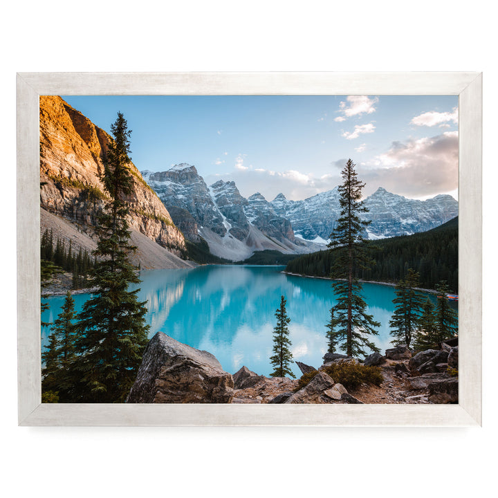 A breathtaking view of a serene mountain lake surrounded by towering peaks and lush forests, with a clear blue sky overhead.