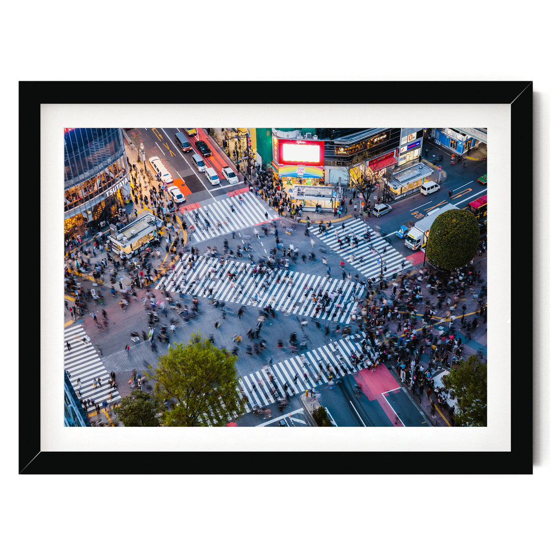 a busy city intersection with a large crowd of people crossing the street, surrounded by tall buildings and illuminated by colorful lights.