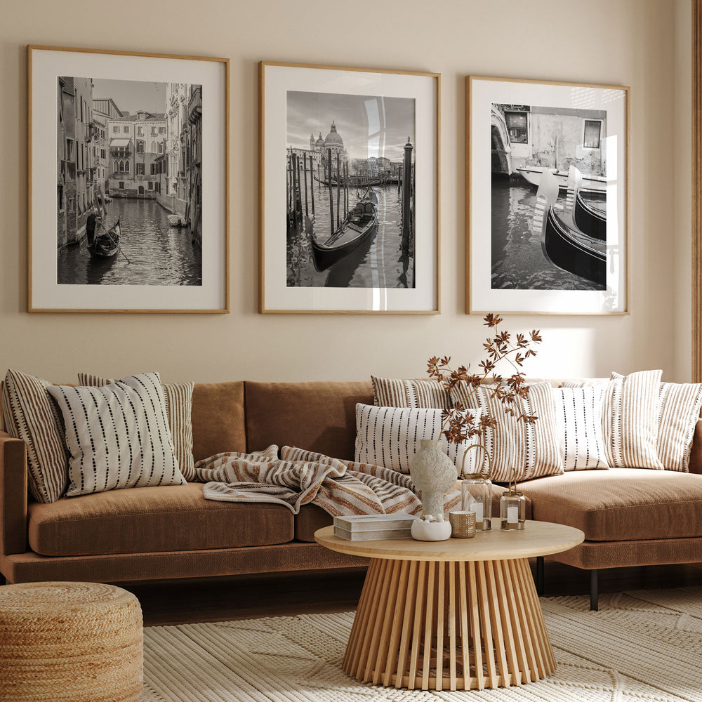 a living room with a brown sofa, a wooden coffee table, and three framed black and white photographs of Venice canal scenes hanging on the wall above the sofa.