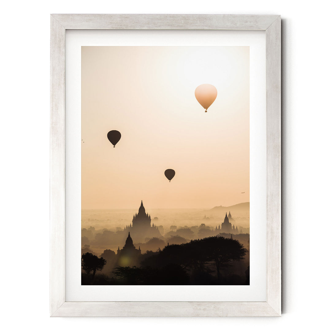 three hot air balloons floating in the sky above a cityscape with silhouetted buildings.