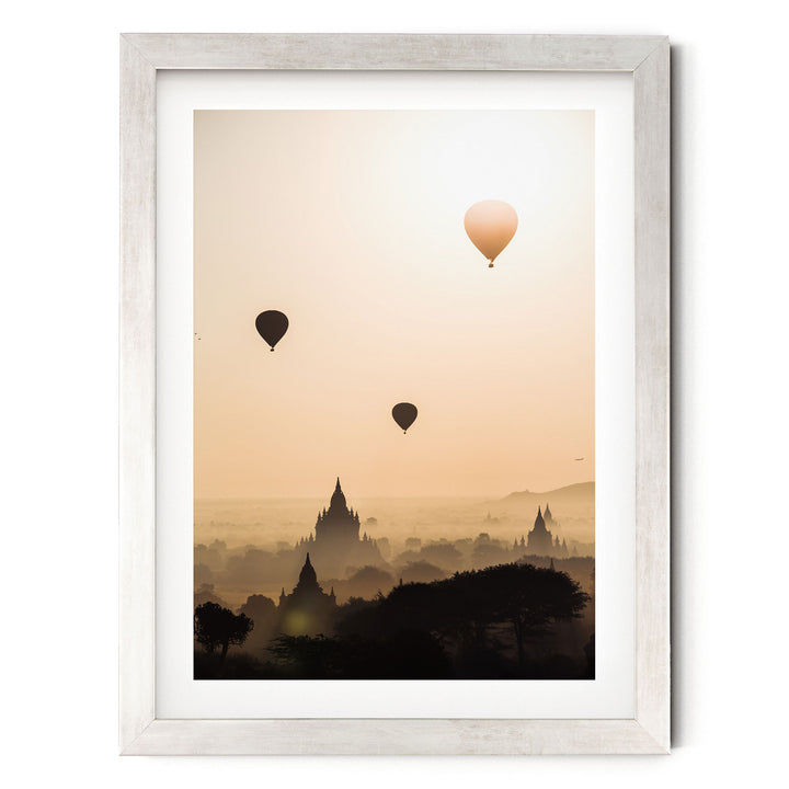 three hot air balloons floating in the sky above a cityscape with silhouetted buildings.