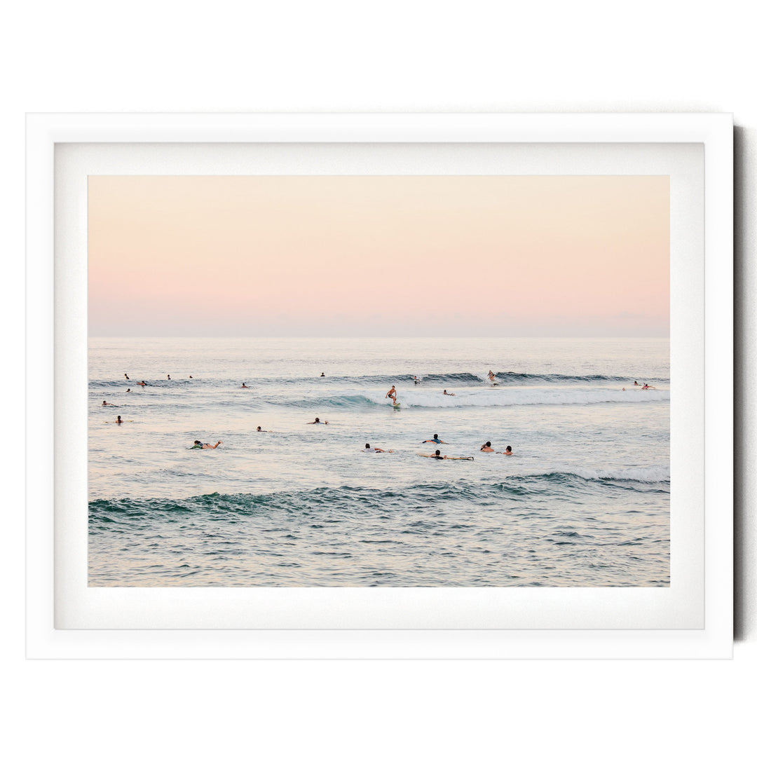 a group of people swimming and surfing in the ocean, with waves visible in the background.