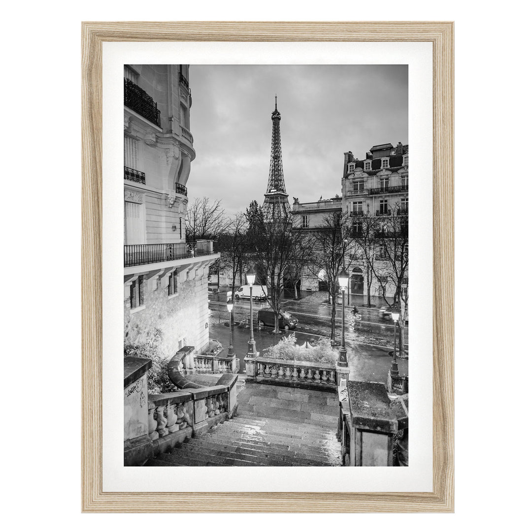 A black and white photograph of the Eiffel Tower in Paris, France, with the surrounding buildings and a wet street visible.