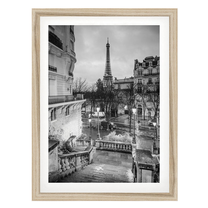 A black and white photograph of the Eiffel Tower in Paris, France, with the surrounding buildings and a wet street visible.