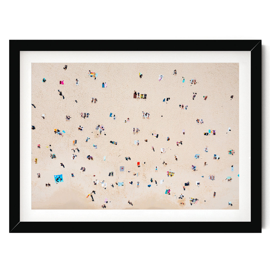 The image is a framed photograph depicting a beach scene with numerous people scattered across the sandy surface.
