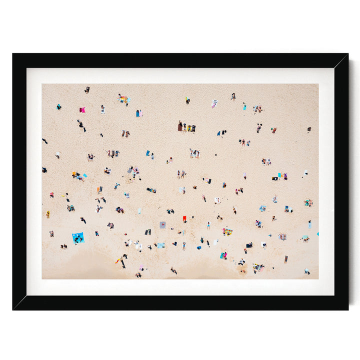 The image is a framed photograph depicting a beach scene with numerous people scattered across the sandy surface.