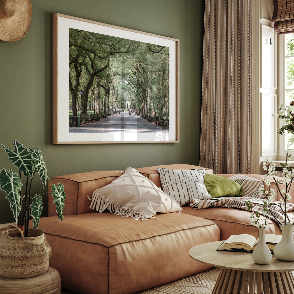 a cozy living room with a large framed picture of a tree-lined street hanging on the wall above a brown leather sofa adorned with throw pillows.
