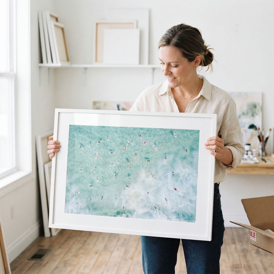 Woman holding a framed Bondi Beach surfers print in a studio