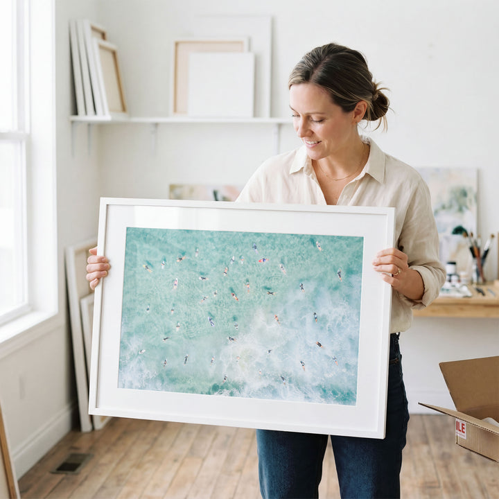 Woman holding a framed Bondi Beach surfers print in a studio