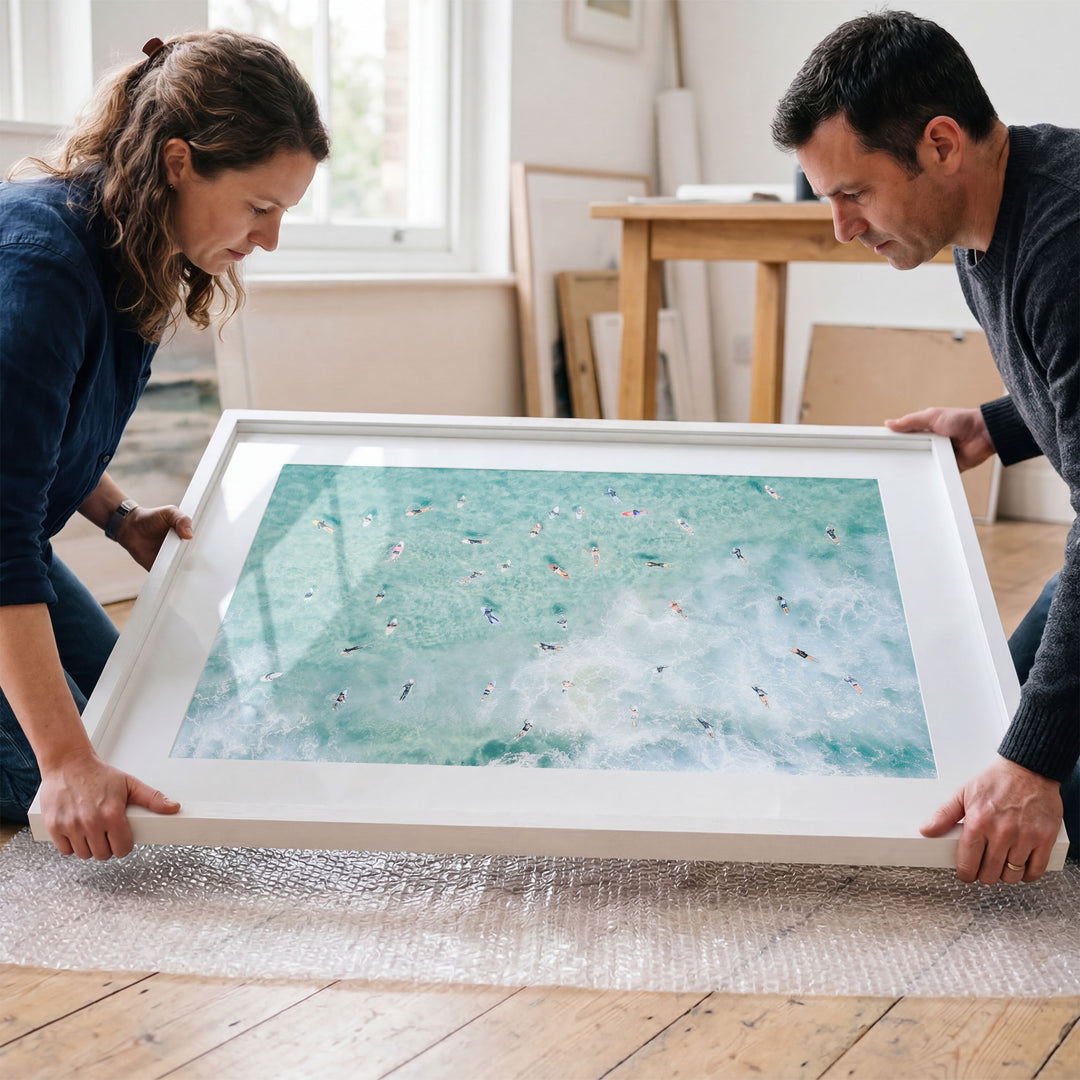 Couple placing a framed Bondi Beach surfers print in a room