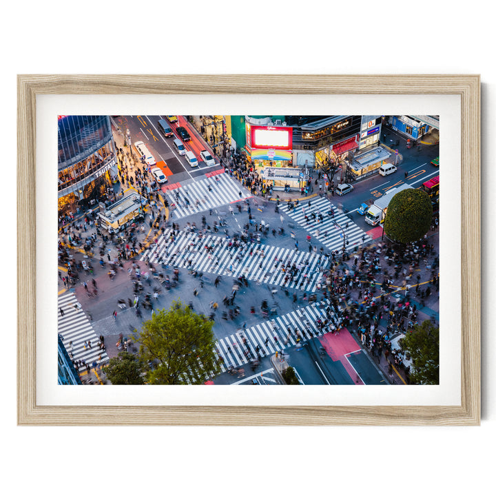 a busy city intersection with a large crowd of people crossing the street, surrounded by various vehicles and buildings.