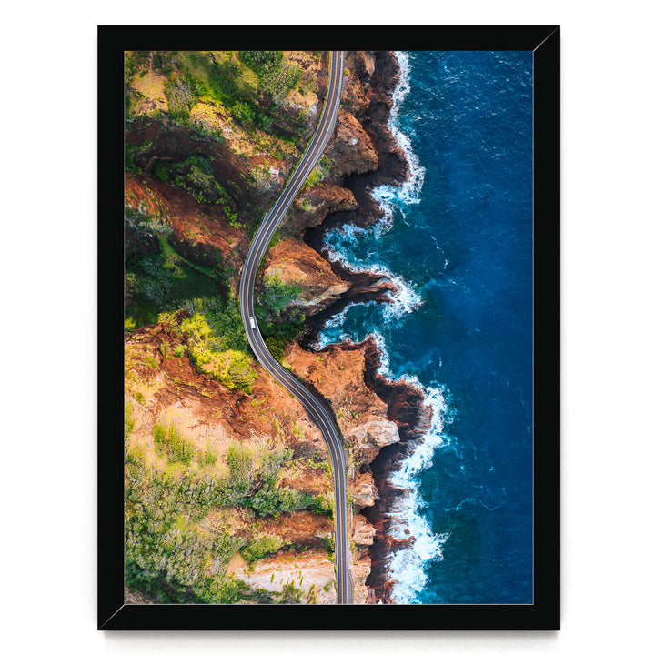 The image is an aerial view of a winding road cutting through a rugged coastline with cliffs and the ocean.