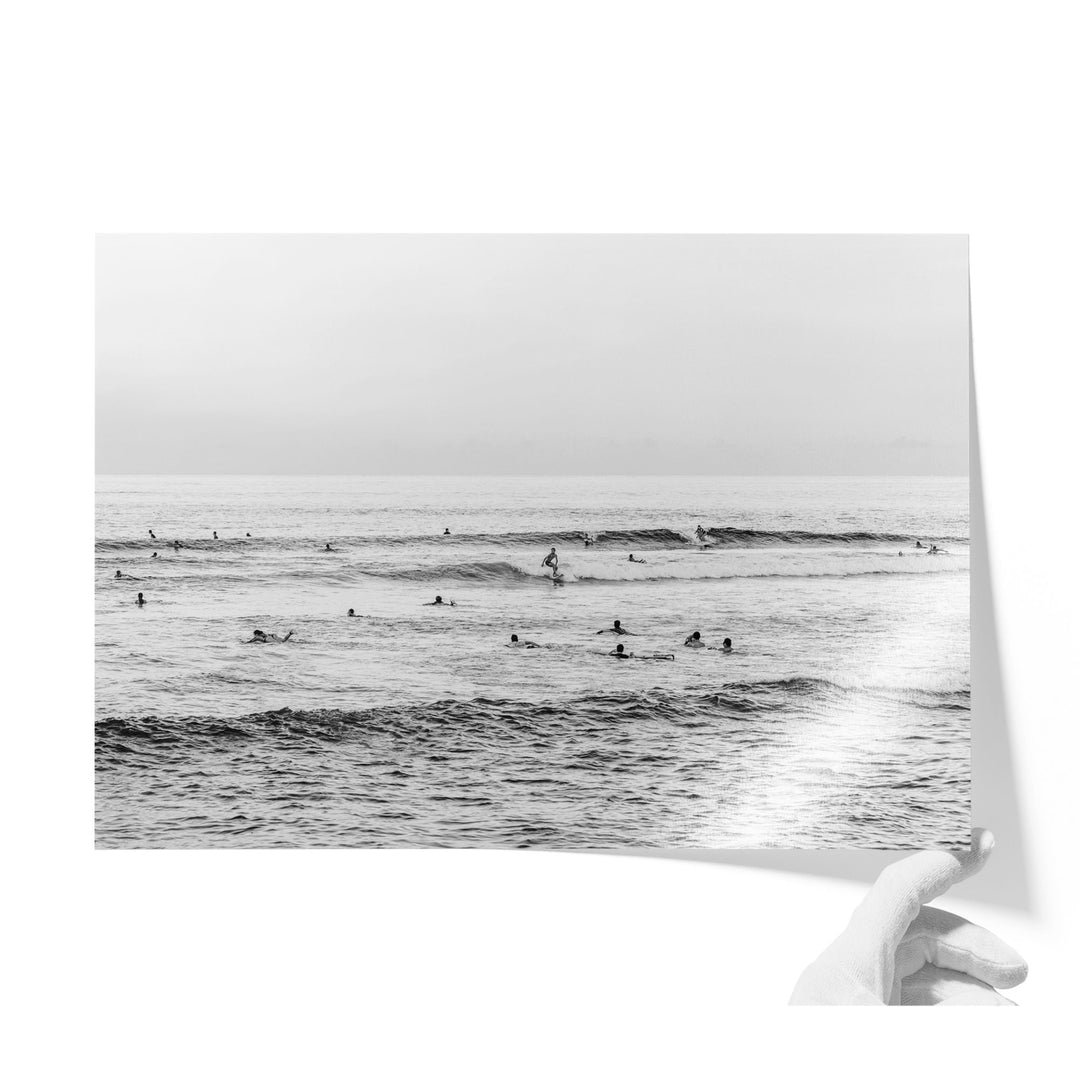 A black and white photograph of a group of people swimming and surfing in the ocean, with waves visible in the background.