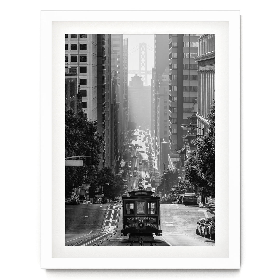 A black and white photograph of a trolley car traveling down a busy city street, surrounded by tall buildings and traffic.