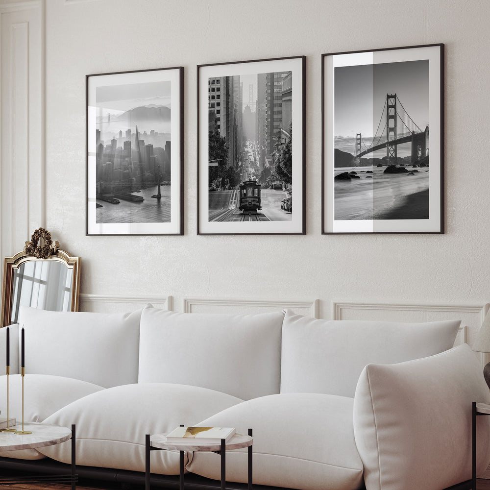 a living room with a white sofa and a mirror on the wall. Above the sofa, there are three framed black and white photographs of iconic landmarks, including the Golden Gate Bridge and the San Francisco skyline.
